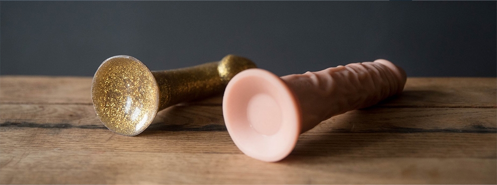 Ahşap bir masanın üzerinde yan yana duran, iki farklı vantuzlu dildo.