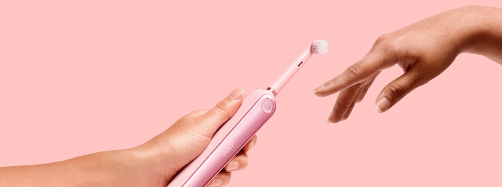 Açık pempe bir arkaplan üzerinde bir elden diğerine uzatılan diş fırçası.