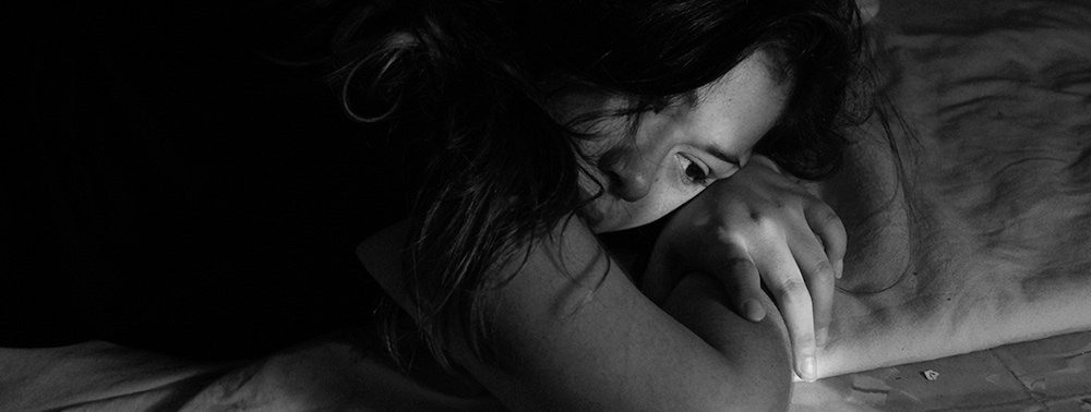 Yüz üstü yatan üzgün bir kadının siyah-beyaz fotoğrafı.